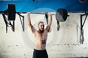 Brutal muscular man with beard train with barbell raised over head in gym