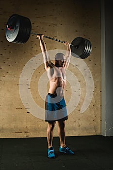 Brutal muscular man with beard train with barbell raised over head in gym