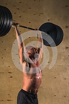 Brutal muscular man with beard train with barbell raised over head in gym