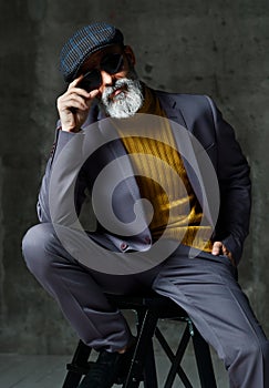 Brutal senior white bearded man in classic grey suit, green sweater, cap and aviator sunglasses stylish fashionable men