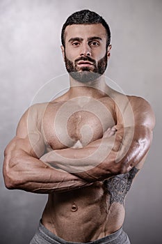 Brutal strong bodybuilder man posing in studio on grey background.