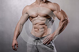 Brutal strong bodybuilder man posing in studio on grey background.
