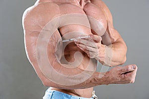 Brutal strong bodybuilder man posing in studio on grey background.