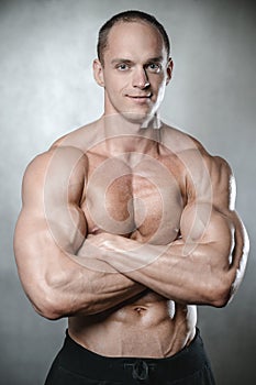 Brutal strong bodybuilder man posing in studio on grey background