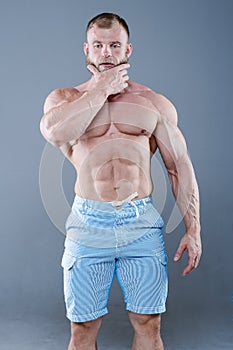 Brutal strong bodybuilder man posing in studio on grey background.