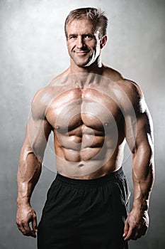 Brutal strong bodybuilder old man posing in studio grey background