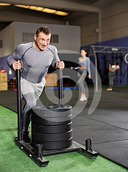 Brutal strong muscular bodybuilder athletic man pumping up muscles with crossfit traction sled in gym. Workout