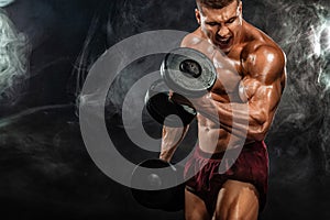 Brutal strong muscular bodybuilder athletic man pumping up muscles with dumbbell on black background. Workout