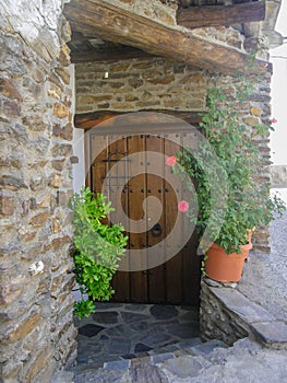 Brwon wooden front door with metal doorknocker stone wall and plants in spain