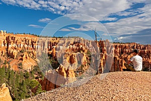 Bryce Canyon - Man sitting on hill with scenic aerial view of hoodoo sandstone rock formations on Queens Garden trail, Utah, USA