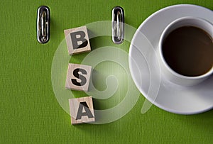 BSA - acronym on wooden cubes against the background of a green folder and a cup of coffee