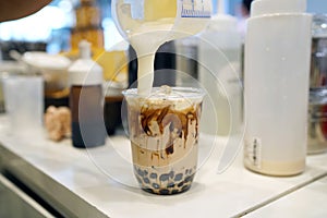 Bubble Milk Tea - Pouring cream cheese into glass of milk tea with black sugar syrup Kuromitsu and hot black pearl Boba topped