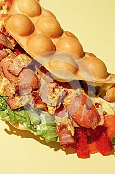 Bubble waffle hot dog with sausage, tomato, lettuce, bacon, sauce, mustard, cheese, red bell pepper isolated on yellow background