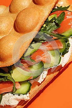 Bubble waffle sandwich with salmon, arugula, lettuce, cream cheese and cucumber  isolated on orange background. Fast food, take