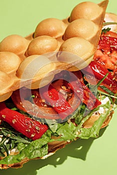 Bubble waffle vegetarian with tomato, lettuce,  sauce, cream cheese, red bell pepper isolated on green background. Fast food, take