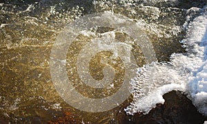 Bubbles and foam on brown river water with ice and snow parts in sunny winter day