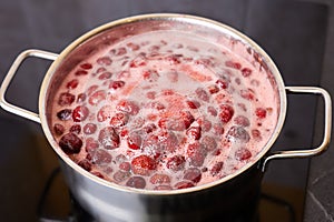 Bubbling red strawberry berries create a vibrant mixture as they simmer in a pot.