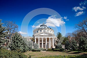 BUCHAREST, ROMANIA - MARCH 18, 2023: Ateneul Roman main facade in front of a park during a sunny afternoon. The Romanian Athenaeum