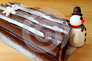 Buche de Noel or Chocolate Yule Log Cake for Christmas Celebration with a Cute Snowman Marzipan on a Wooden Table