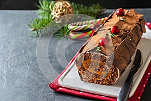 Buche de Noel. Traditional Christmas dessert, Christmas yule log cake with chocolate cream, cranberry. On stone gray