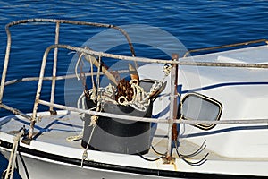 Bucket with anchors, rusty chain and ropes tied to steel railing on front of roofed white fishing boat