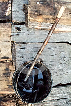 A bucket of black tar boils on the fire for use in repair and waterproofing.