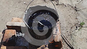 A bucket of boiling resin on bricks. Pieces of bitumen are melted in a bucket using a gas burner. Roof repair.