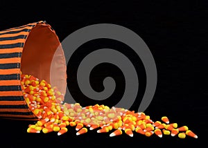 Bucket of candy corn spilling onto black surface and background