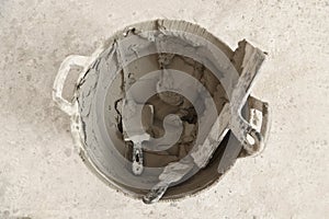 Bucket with cement and putty knifes on floor, top view