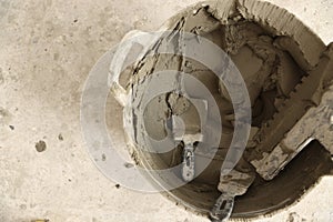 Bucket with cement and putty knifes on floor, top view. Space for text