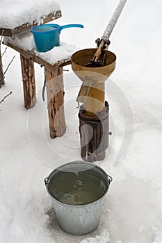 Bucket of clean drinking water stands next to the well and the hand pump in a village courtyard