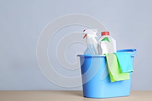 Bucket with cleaning supplies on table against grey background