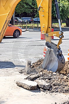 The bucket of a construction excavator undermines the old asphalt on a fenced section of the road to carry out repair work on photo