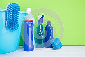 Bucket with different bottles of detergents for cleaning on a green background