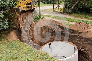 A bucket of excavator with a pile of sand and earth buries sewer concrete rings in the industrial zone