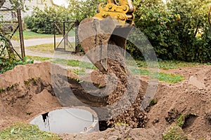 A bucket of excavator with a pile of sand and earth buries sewer concrete rings in the industrial zone