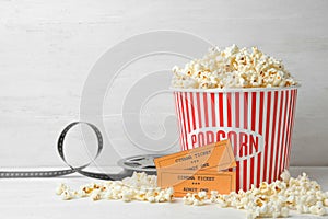 Bucket of fresh popcorn, tickets and movie reel on white table, space for text. Cinema snack