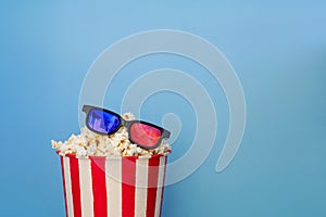 A bucket full of popcorn on a blue background and 3D glasses