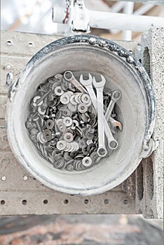 A bucket full of wrenches, washers and stud bolts is placed on the scaffolding