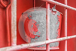 A bucket of galvanized iron with red peeling paint in an old fire box equipment and tools to help in safely extinguishing a fire