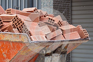 The bucket of a mini loader, which carries a fully loaded red brick down the street. An example of solving problems with low costs