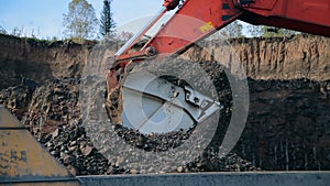 A bucket of red excavator loads a dump truck