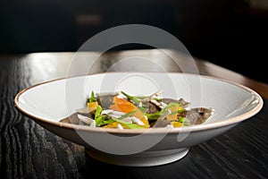 Buckwheat dumplings with fresh mushrooms served on a white plate over black background.