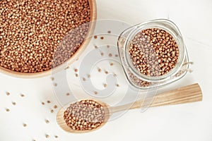 Buckwheat kernels in a glass jar, wooden bowl and spoon on white background. Top view. Copy, empty space for text