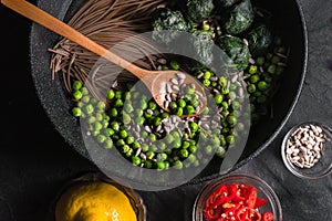 Buckwheat noodles in a frying pan, frozen peas and spinach, chillies and seeds in a bowl