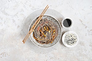 Buckwheat noodles with vegetables and meat decorated with sesame and seaweeds in bowl on grey background. Top view