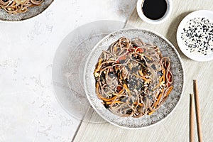 Buckwheat noodles with vegetables and meat decorated with sesame and seaweeds in bowls on grey background