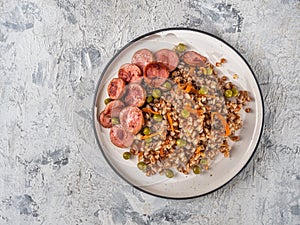 Buckwheat porridge with onions and carrots, fried sausage and green peas for a light breakfast