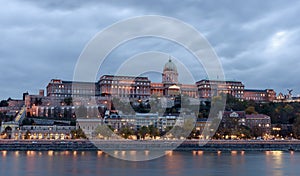 Buda Castle, overlooking the river Danube, in Budapest. It is early evening, and the castle is lit up