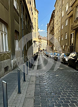Budapest downtown business area shows car parking on the cobblestone narrow street and pedestrian traffic.